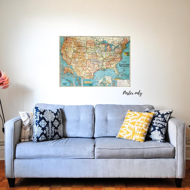 May include: A vintage map of the United States of America with a blue background and brown lines. The map is framed and hanging on a white wall above a light blue sofa with patterned cushions.