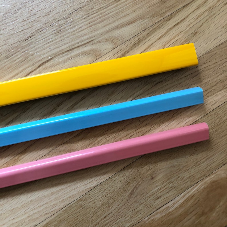 May include: Three long, thin, rectangular pieces of trim in yellow, light blue, and pink. The trim is made of a smooth, hard material and has a slightly rounded edge.
