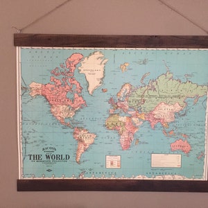 Pu&ograve; includere: Una mappa del mondo vintage con sfondo blu e continenti in vari colori. La mappa &egrave; incorniciata in una cornice di legno scuro ed &egrave; appesa a un muro. La mappa &egrave; intitolata "Bacon's Standard The World On Mercator's Projection".
