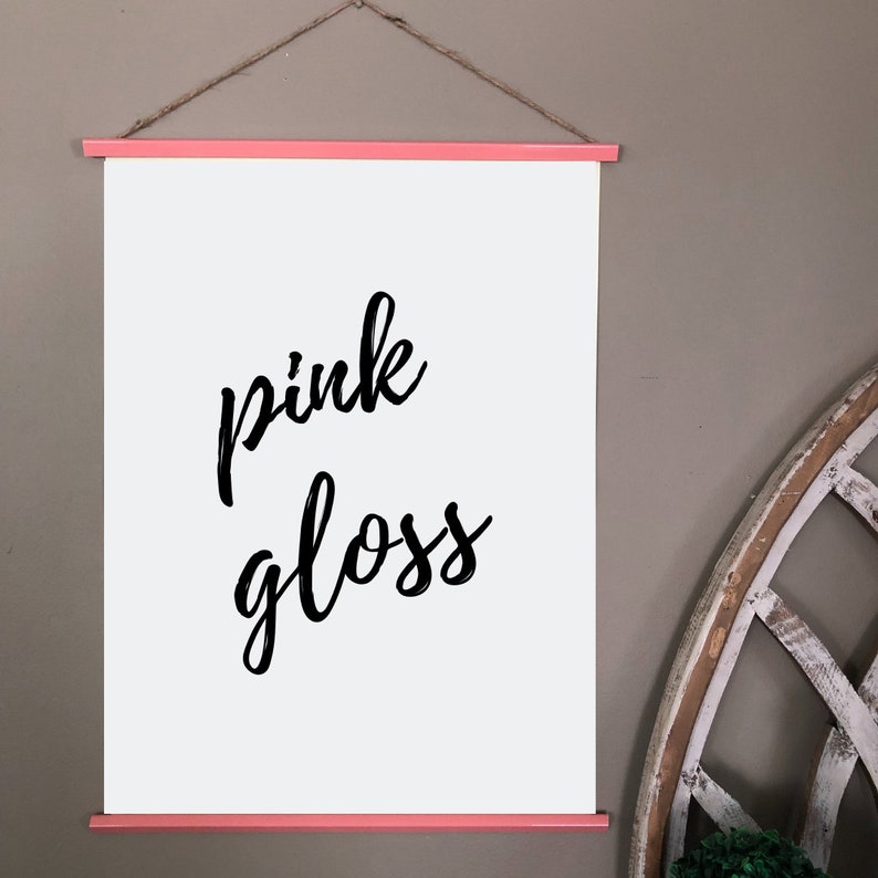 Pu&ograve; includere: Una tela bianca con una cornice in legno rosa, appesa a un muro. La tela ha una calligrafia nera che dice "pink gloss".