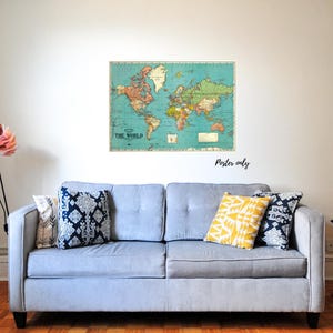 Pu&ograve; includere: Un poster di mappa del mondo vintage con sfondo blu e continenti colorati. La mappa &egrave; incorniciata e appesa a una parete bianca sopra un divano blu chiaro con cuscini a motivi.