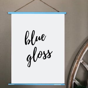 Pu&ograve; includere: Una tela bianca con una cornice blu, appesa a un muro. La tela ha le parole "blue gloss" scritte in corsivo nero.