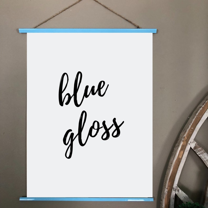 May include: A white poster with the words "blue gloss" in black script lettering. The poster is held by light blue wooden bars at the top and bottom, suspended by a natural twine string.