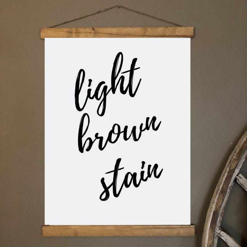 May include: A white canvas print with the words "light brown stain" in black script. The print is held by wooden bars at the top and bottom, suspended by a thin, brown string.