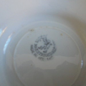 May include: Close-up of the bottom of a white ceramic saucer with a blue and white logo that reads "Made in Austria 1947".