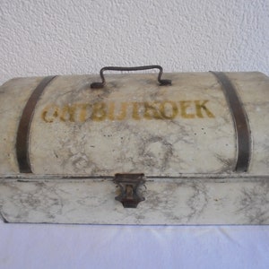 May include: An antique, off-white metal chest with a curved top and a handle. The chest has a marble-like pattern and is accented with dark metal bands and a clasp. The word "ONTBIJTBROEK" is printed in gold lettering on the top.