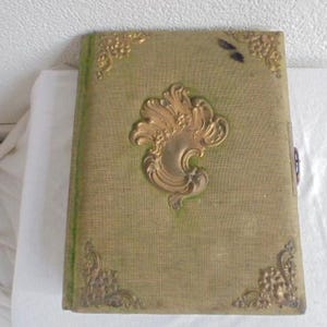 Op de afbeelding: Een vintage groen fotoalbum met gouden reliëfmotieven van bloemen en een decoratieve sluiting. Het album is gesloten en heeft een textuurrijke stoffen omslag.
