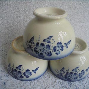 May include: Three white ceramic bowls with blue floral designs. The bowls are stacked on top of each other.
