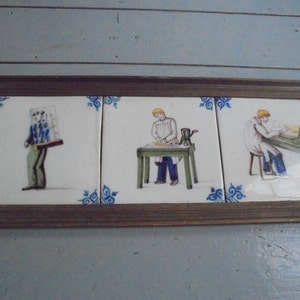 Könnte beinhalten: Drei antike Keramikfliesen in einem Holzrahmen. Jede Fliese zeigt eine Person in einem anderen Beruf. Die erste Fliese zeigt eine Person, die eine große Kiste trägt, die zweite Fliese zeigt eine Person, die an einem Tisch mit einer Schleifmaschine arbeitet, und die dritte Fliese zeigt eine Person, die an einem Tisch mit einer Säge arbeitet.