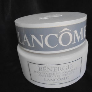 Op de afbeelding: Een witte pot Lancôme Renergie gezichtscrème. De pot heeft een blauw etiket met de tekst "Lancôme" en "Renergie Soin Double Performance Anti-Rides et Fermete Lancôme Paris".
