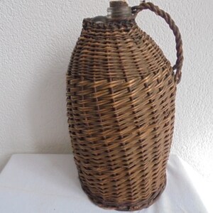 May include: A brown wicker-wrapped glass bottle with a woven handle. The bottle is oval-shaped and has a clear glass top.