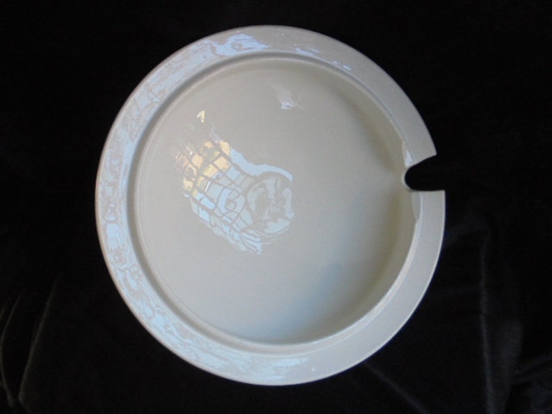 May include: White ceramic serving dish with a decorative design around the edge. The dish has a small spout on the side.