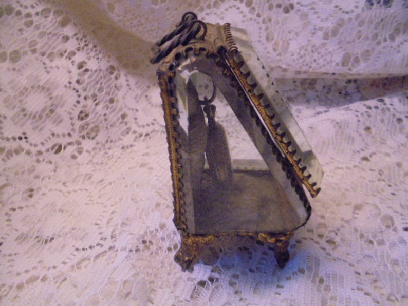 May include: A gold-toned glass display case with a beveled glass front and ornate metal trim. The case is open and empty.
