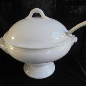 May include: White porcelain serving bowl with a lid and a ladle. The bowl has a round base and two handles on the sides. The lid has a knob on top.