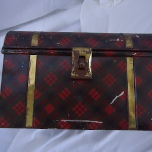May include: A vintage metal tin box with a red and black plaid pattern and gold trim. The box has a hinged lid and a latch.