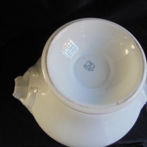 May include: White ceramic serving bowl with two handles shaped like stylized animal heads. The bowl has a raised rim and a smooth, glossy finish. The bottom of the bowl has a circular mark with the text "Made in England" inside.