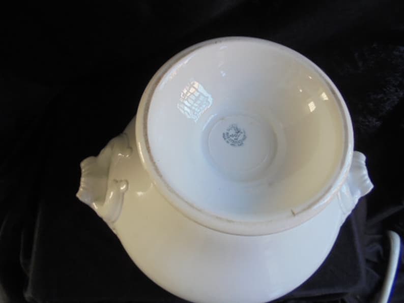 May include: White ceramic serving bowl with two handles shaped like stylized animal heads. The bowl has a raised rim and a smooth, glossy finish. The bottom of the bowl has a circular mark with the text "Made in England" inside.
