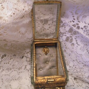 May include: A vintage glass and gold-toned jewelry box with a padded interior. The box has a hinged lid and is decorated with ornate details.