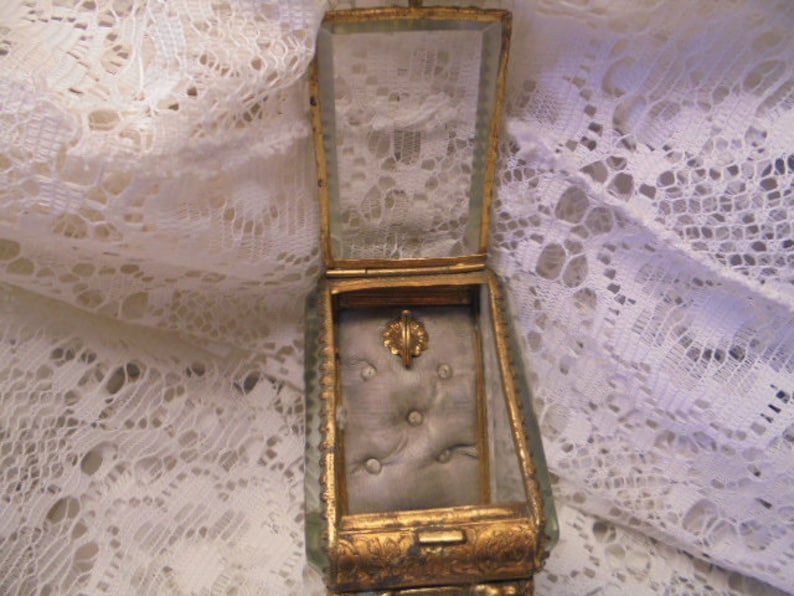 May include: A vintage glass and gold-toned jewelry box with a padded interior. The box has a hinged lid and is decorated with ornate details.