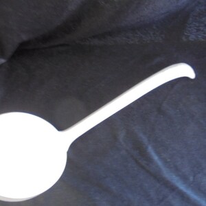 May include: A white ceramic ladle with a long handle. The ladle is a kitchen utensil used for serving soup, stew, or other liquids.