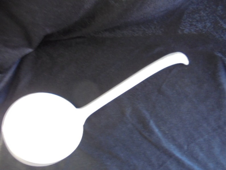May include: A white ceramic ladle with a long handle. The ladle is a kitchen utensil used for serving soup, stew, or other liquids.