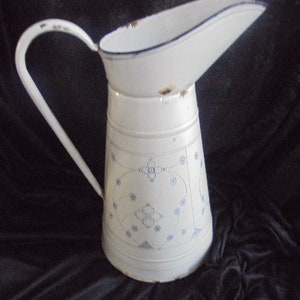 May include: White enamel pitcher with a blue and white floral design. The pitcher has a wide spout and a handle.