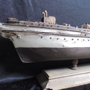 Può includere: Un modello di nave in legno vintage dipinto di bianco e nero, con uno scafo dettagliato e una base in legno. Il modello di nave ha un aspetto invecchiato, il che suggerisce che si tratti di un antico.