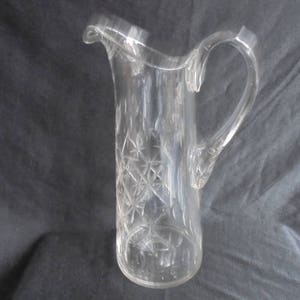 Può includere: Un'ampia brocca di vetro trasparente con un design in vetro tagliato. La brocca ha un'ampia apertura e un manico.