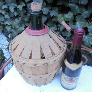 May include: A vintage wicker-covered wine bottle with a cork stopper and a red label. A bottle of red wine with a label that reads "Saint Aubin 1er Cru" is in the foreground.