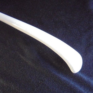 May include: A white ladle with a long, curved handle. The ladle is made of metal and has a smooth, polished finish.