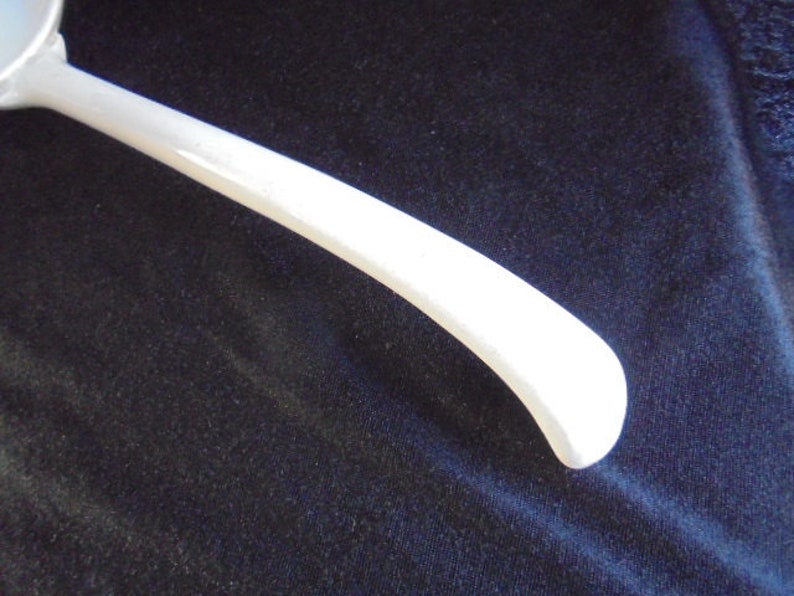 May include: A white ladle with a long, curved handle. The ladle is made of metal and has a smooth, polished finish.