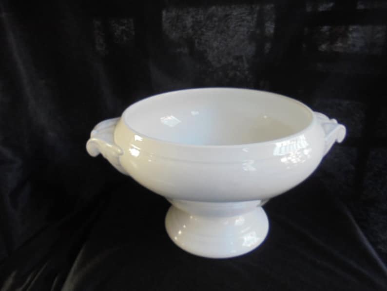 May include: A white porcelain serving bowl with two handles and a pedestal base.