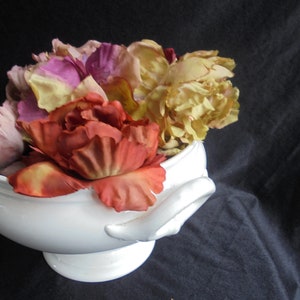 May include: A white ceramic bowl filled with a variety of artificial flowers, including pink, yellow, and orange roses.