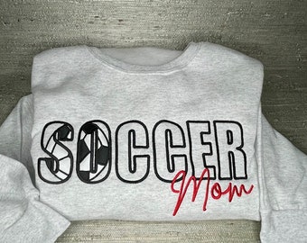 May include: Gray sweatshirt with black and white soccer ball design and the text "SOCCER Mom" in red.