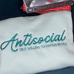 May include: A light blue sweatshirt with the text "Antisocial (But Willing to Discuss Books)" embroidered in teal.