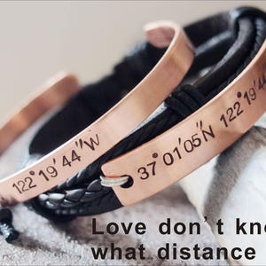 May include: Two copper bracelets with black leather bands. One bracelet has the coordinates "37&deg;01'05'N 122&deg;19&prime;44" engraved on it. The other bracelet has the coordinates "122&deg;19&prime;44&Prime;W" engraved on it. The bracelets are on a wooden surface. The text "Love don't know what distance is" is written below the bracelets.