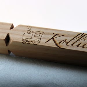 May include: A wooden whistle with a train design and the name "Kollier" engraved on it.