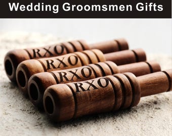 May include: Close-up of several wooden cigar-shaped objects with the letters "RXO" engraved on them. The objects are arranged in a row, with the text "Wedding Groomsmen Gifts" at the top.
