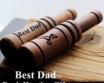 May include: Two cylindrical wooden duck calls with a smooth finish. One call features the engraved text Best Dad and a duck silhouette. The other call displays a detailed engraved duck in flight. Both items have horizontal grooves along the body.