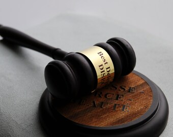 May include: A black wooden gavel with a gold-colored metal band engraved with the text Best Delegate DISEC. The gavel rests on a circular wooden base featuring a dark wood grain center with the engraved text ESSE- RCE- EAUTÉ.