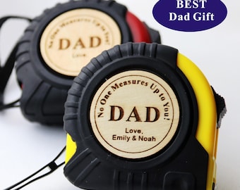 May include: Two retractable tape measures with black and yellow casings. Each features a circular wooden inlay engraved with the text "No One Measures Up to You! DAD Love, Emily & Noah". A blue oval graphic in the corner displays "BEST Dad Gift".