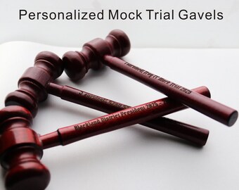May include: Several dark red wooden gavels are displayed, some overlapping. The text "Personalized Mock Trial Gavels" is at the top. The gavels have engraved text on the handles, including "Isurowed, Tray er mark Trial 2020" and "Blackland District President 2925-2".