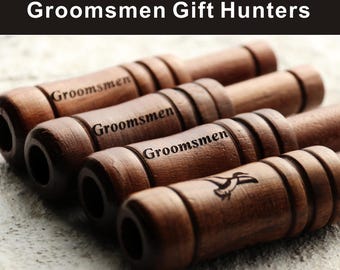 May include: Close-up of several wooden duck calls with the word "Groomsmen" engraved on them. One call features a bird graphic. The text "Groomsmen Gift Hunters" is at the top.