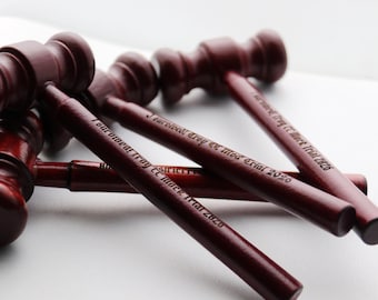 May include: A collection of dark red wooden gavels, some with text reading "I survived Troy CC Mock Trial 2020". The gavels are arranged on a white surface, with some in focus and others blurred.