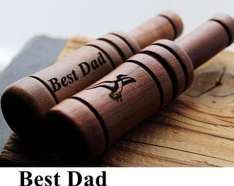 May include: Two cylindrical wooden duck calls with a dark brown finish. One call features the engraved text "Best Dad" and the other displays a laser-engraved graphic of a flying duck. Both items have horizontal grooves carved into the wood.