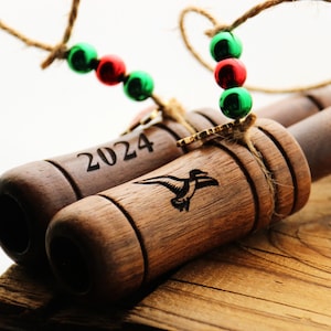 May include: Two wooden ornaments with a string of red and green beads. One ornament is engraved with the year 2024 and the other has a stylised image of a duck.