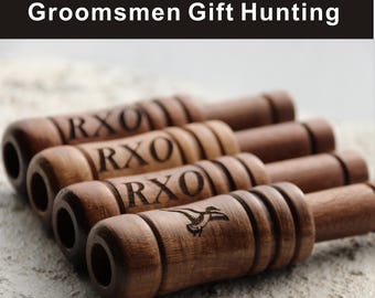 May include: Four wooden duck calls with the text "RXO" engraved on them. One call features a duck graphic. The calls are brown and arranged on a light-colored surface. The text "Groomsmen Gift Hunting" is at the top.