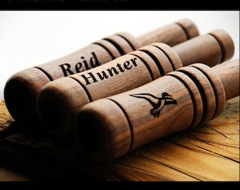 May include: Three cylindrical wooden duck calls with dark brown grain. The calls are engraved with the names Reid and Hunter, and a flying duck silhouette. The text Mens Gifts and Duck Hunting Gifts appears in white on black bars at the top and bottom.