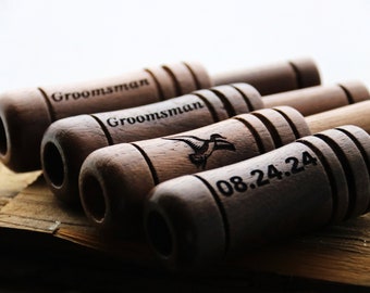 May include: Five wooden shotgun shell wedding favors with engraved text. The text includes "Groomsman" and a date, "08.24.24". One of the favors also has a small engraved image of a bird in flight.