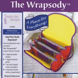 May include: The Wrapsody bag, a cross-body or shoulder style purse, features a colorful striped design. The bag has a yellow interior, red exterior, and purple trim. Dimensions are 25.4cm x 14cm x 16.5cm tall.